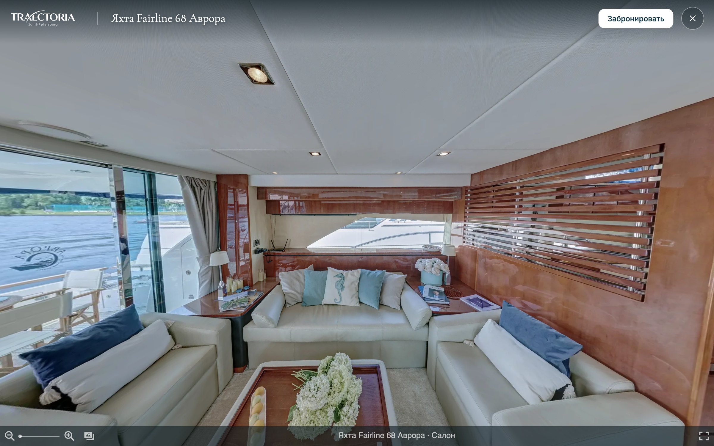 3D-тур яхты Fairline 68 «Аврора», точка «Салон»: светлые диваны, столик с цветами, деревянные панели и окна на воду